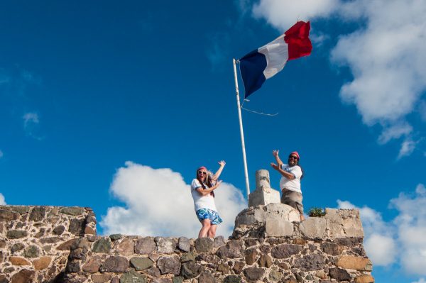 Les co-fondateurs de l'association Les Fruits de Mer posent sous un drapeau du nouveau logo de l'association à Fort Louis à Marigot.